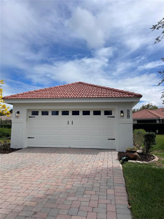 A detached garage with a white door, tiled roof, and paver driveway under a cloudy sky — 319 NIBLICK CIRCLE, WINTER HAVEN, FL