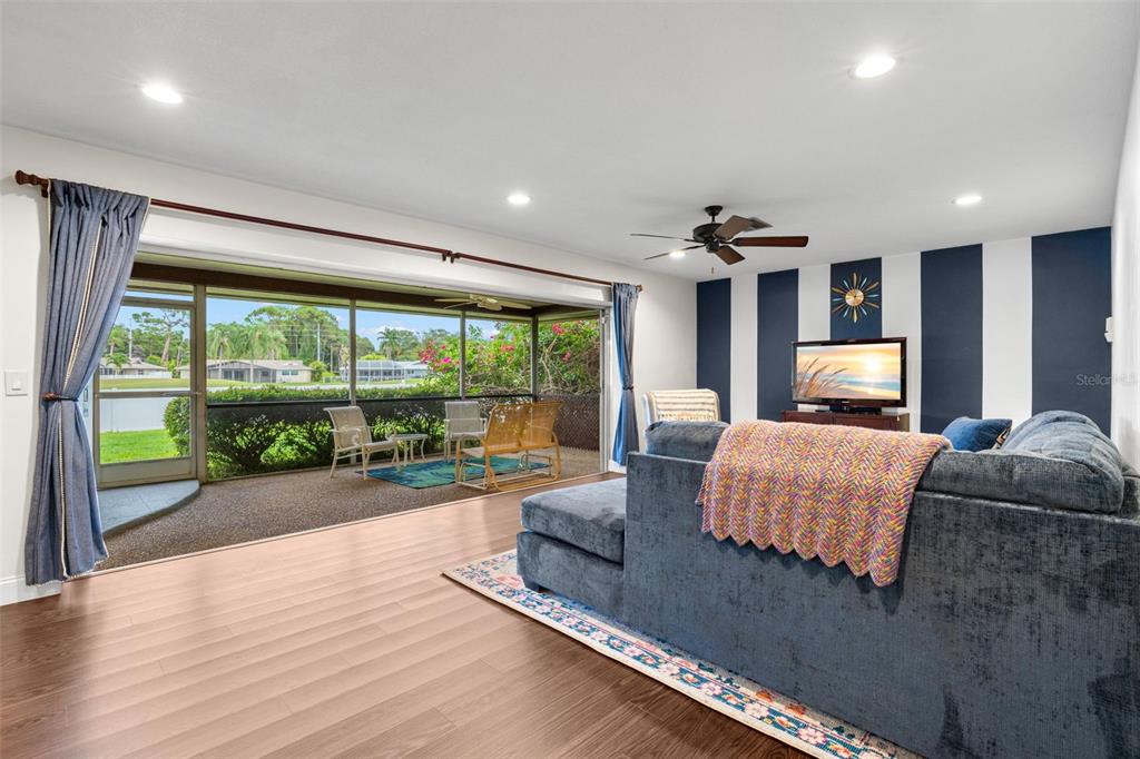 A living room with wood-look flooring, a blue sectional, and sliding doors to a screened lanai — 6729 TEQUESTA DRIVE, SEMINOLE, FL
