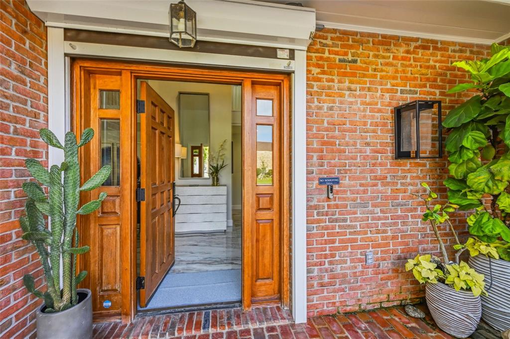 An open wooden front door reveals an entryway with a white dresser and brick exterior — 1307 RIVERVIEW CIRCLE, BRADENTON, FL
