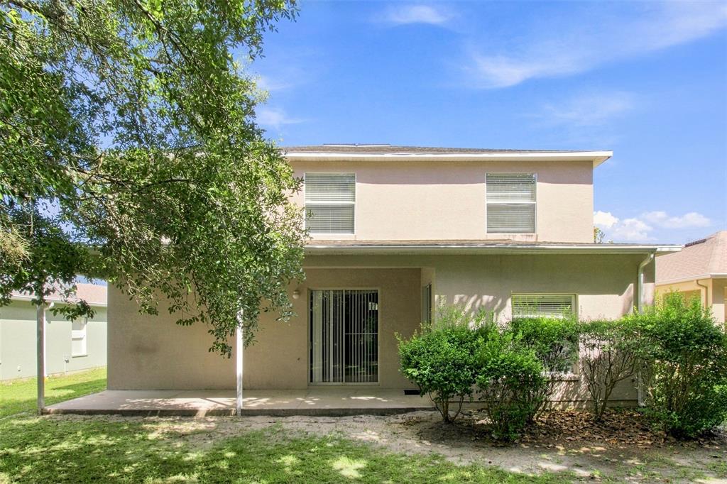 The rear exterior of a two-story house features a concrete patio and a sliding glass door — 4276 BRAEMERE DRIVE, SPRING HILL, FL