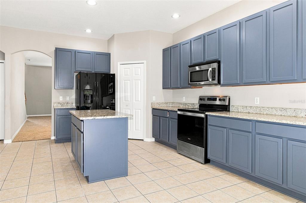 A kitchen features blue cabinets, granite countertops, stainless steel appliances, and a central island — 4276 BRAEMERE DRIVE, SPRING HILL, FL