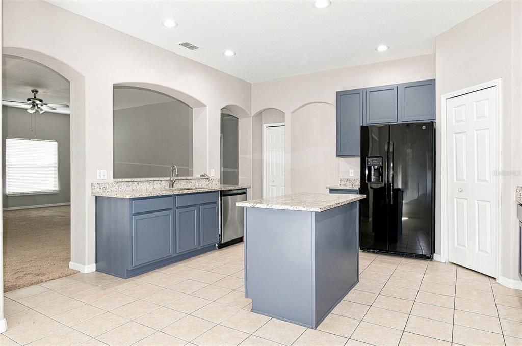 A kitchen with blue cabinets, granite countertops, a center island, and a black refrigerator — 4276 BRAEMERE DRIVE, SPRING HILL, FL
