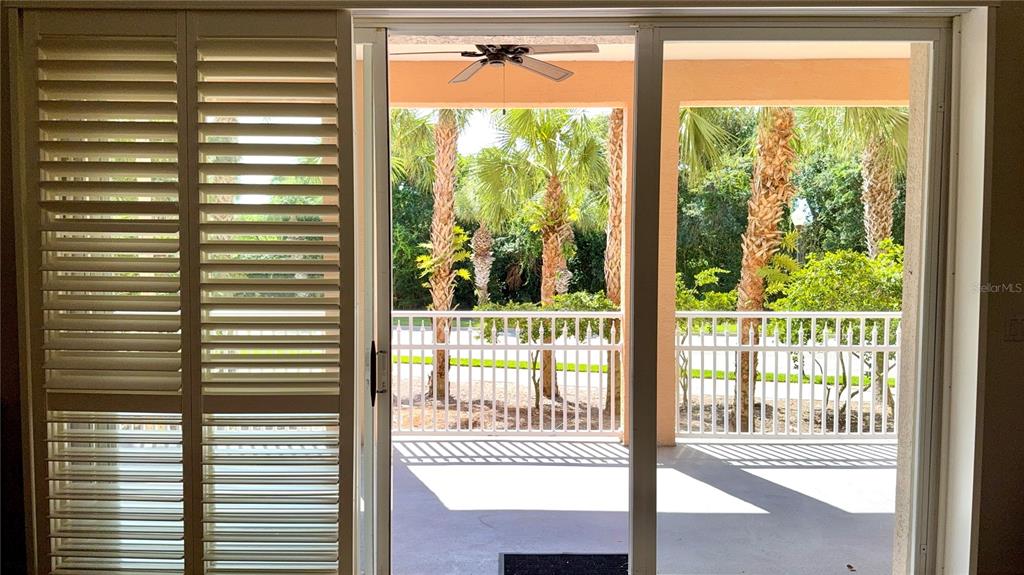 A view through a sliding glass door onto a screened-in patio with palm trees — 35 OCEAN CREST WAY UNIT 1113, PALM COAST, FL
