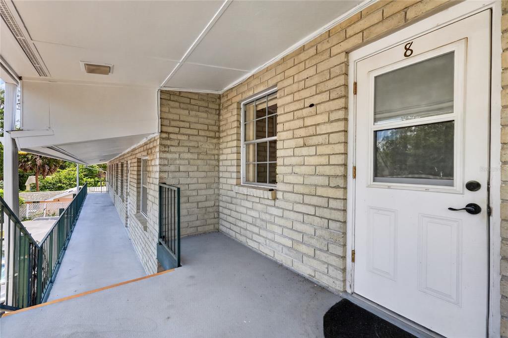 An exterior walkway leads to the entrance of unit 8, featuring a brick wall and railing — 200 E 10TH AVENUE UNIT 8, MOUNT DORA, FL