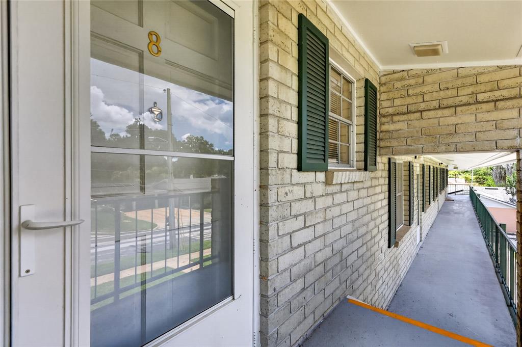 A view of an apartment building exterior walkway with brick walls and green shutters — 200 E 10TH AVENUE UNIT 8, MOUNT DORA, FL