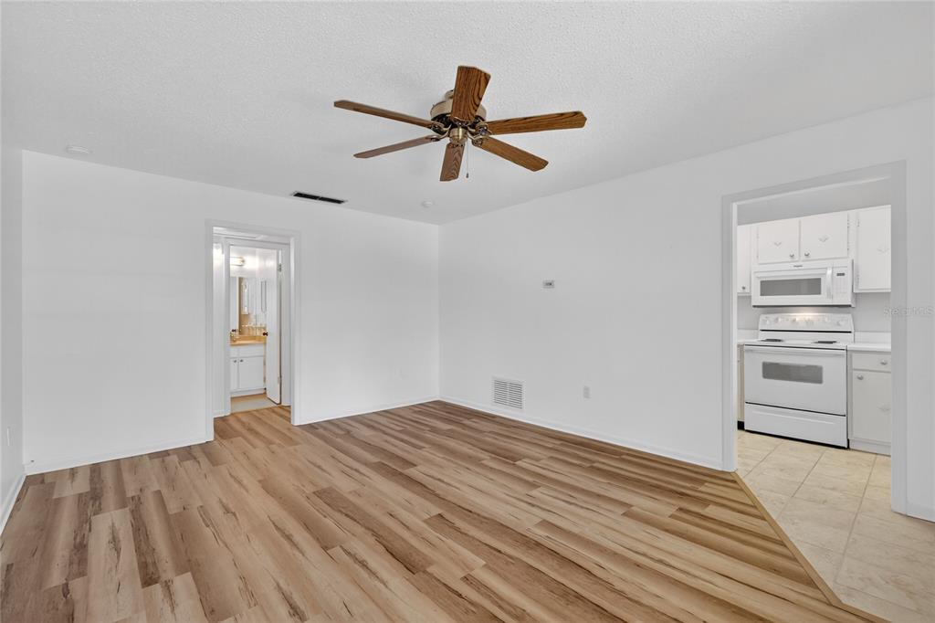 A living room with wood-look flooring, a ceiling fan, and an adjacent kitchen and bathroom — 200 E 10TH AVENUE UNIT 8, MOUNT DORA, FL