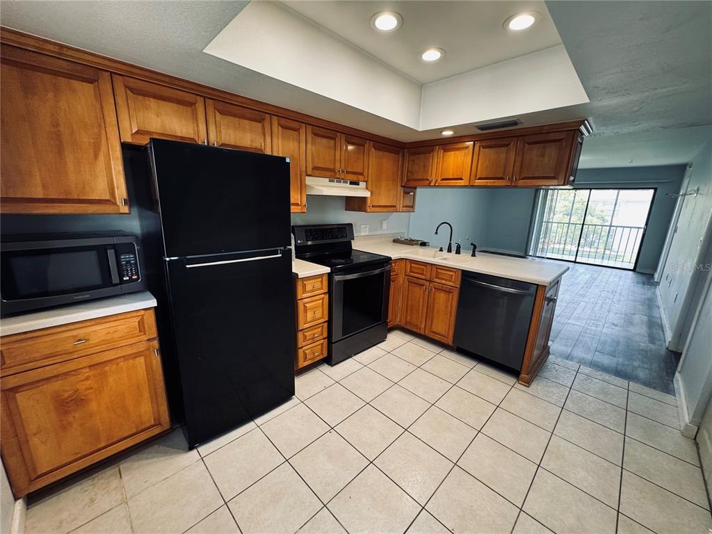A kitchen features wood cabinets, black appliances, tile flooring, and a recessed ceiling light — 106 WINDWARD PLACE, OLDSMAR, FL