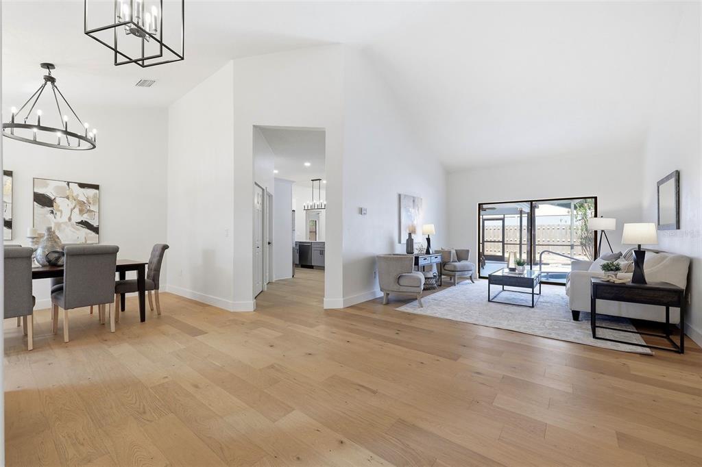 An open-concept living and dining area with light wood floors, white walls, and vaulted ceilings — 3040 WINDRIDGE OAKS DRIVE, PALM HARBOR, FL