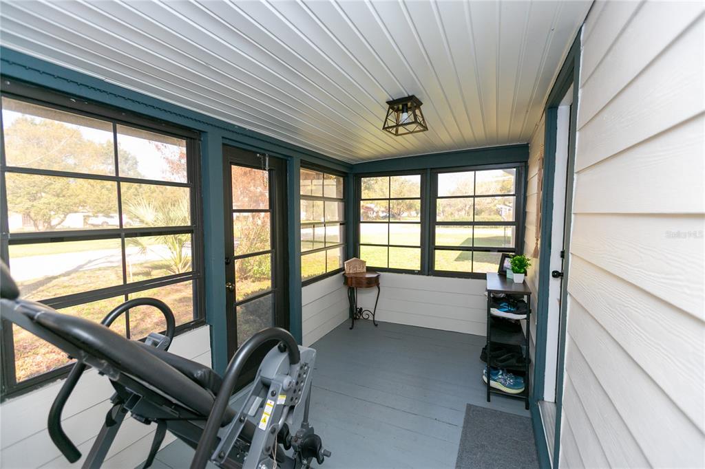 A screened-in porch features gray painted wood flooring, white siding, and a black ceiling light — 807 TENNESSEE AVENUE, ST CLOUD, FL