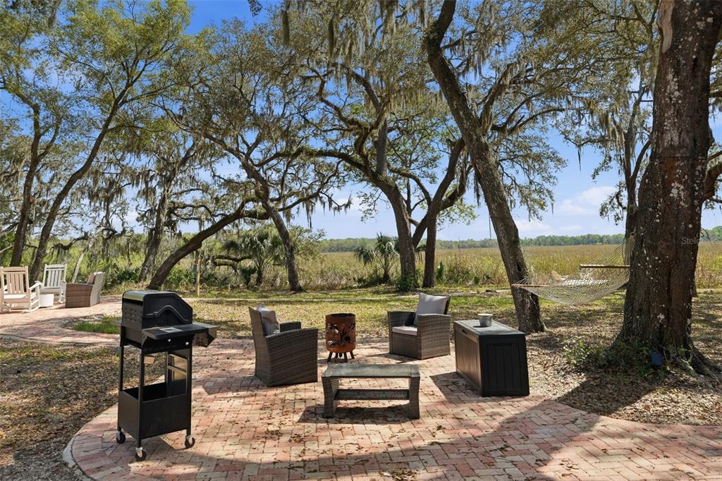 A brick patio features a grill, outdoor seating, and a hammock under large oak trees — 7570 E RINGER COURT, INVERNESS, FL