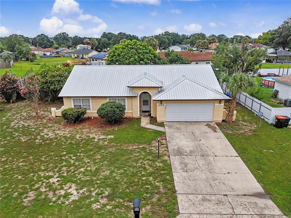 An aerial view of a single-story house with a metal roof and concrete driveway — 306 OAK TRACK RADIAL, OCALA, FL