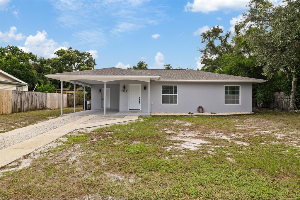 A single-story gray house with a white front door and a covered carport area — 7156 SPRING HILL DRIVE, SPRING HILL, FL