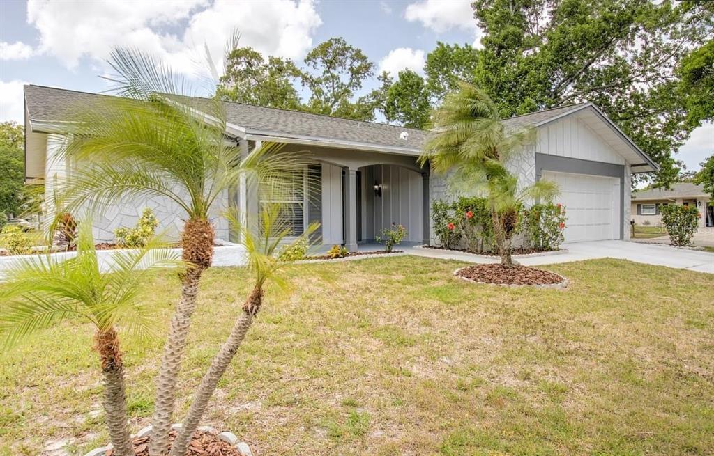 A single-story house with a white stone facade, a gray garage, and palm trees outside — 13309 SHADBERRY LANE, HUDSON, FL