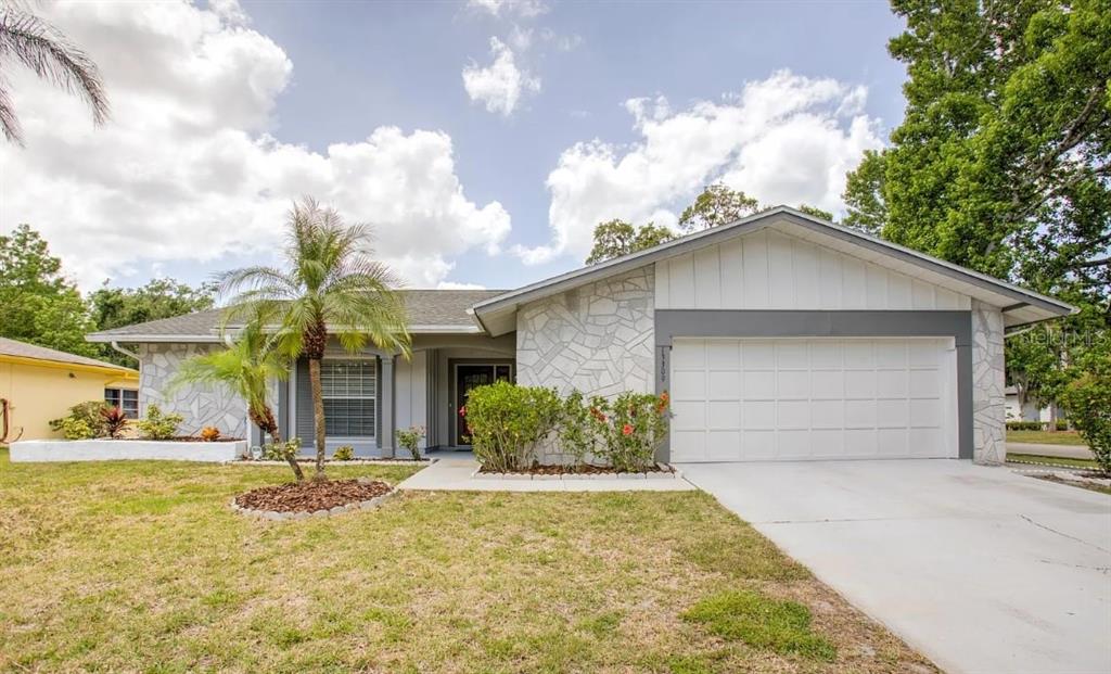 A single-story house with a white stone facade, a two-car garage, and a palm tree — 13309 SHADBERRY LANE, HUDSON, FL