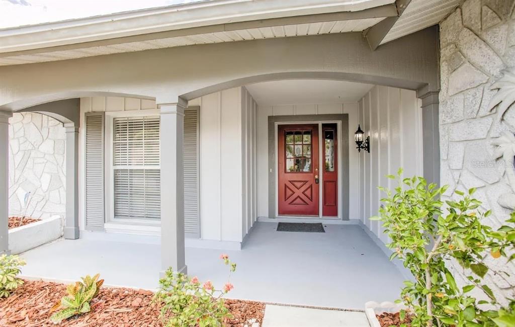 A covered front porch features a red door, white board-and-batten siding, and stone accents — 13309 SHADBERRY LANE, HUDSON, FL