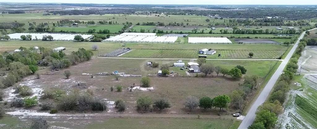 An aerial view shows a rural property with several buildings, greenhouses, and surrounding farmland — 30620 TAYLOR GRADE ROAD, DUETTE, FL