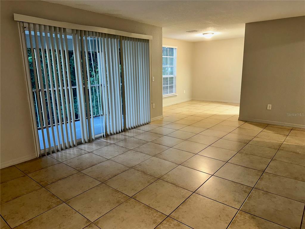 An empty room with beige tile flooring, vertical blinds on a sliding door, and recessed lighting — 4184 VERSAILLES DRIVE UNIT 4184D, ORLANDO, FL