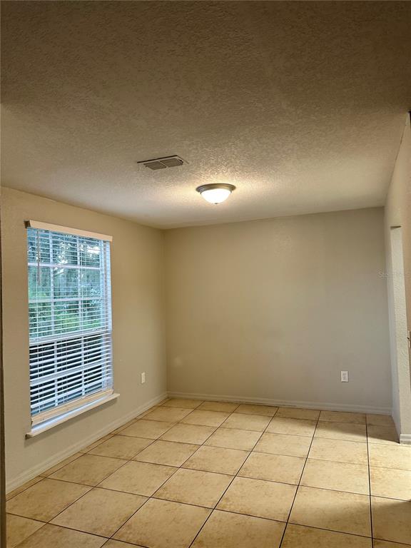 An empty room features beige walls, a tiled floor, a window with blinds, and a ceiling light — 4184 VERSAILLES DRIVE UNIT 4184D, ORLANDO, FL