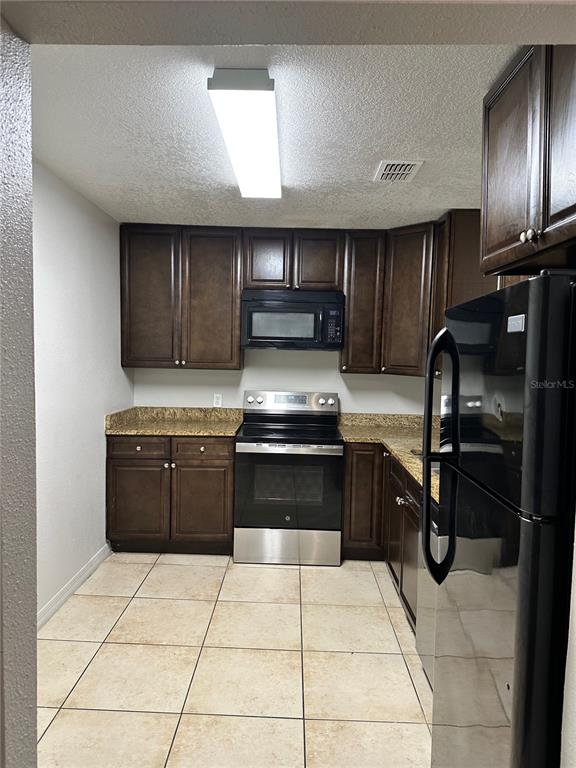 A kitchen features dark wood cabinets, granite countertops, stainless steel appliances, and beige tile flooring — 4184 VERSAILLES DRIVE UNIT 4184D, ORLANDO, FL
