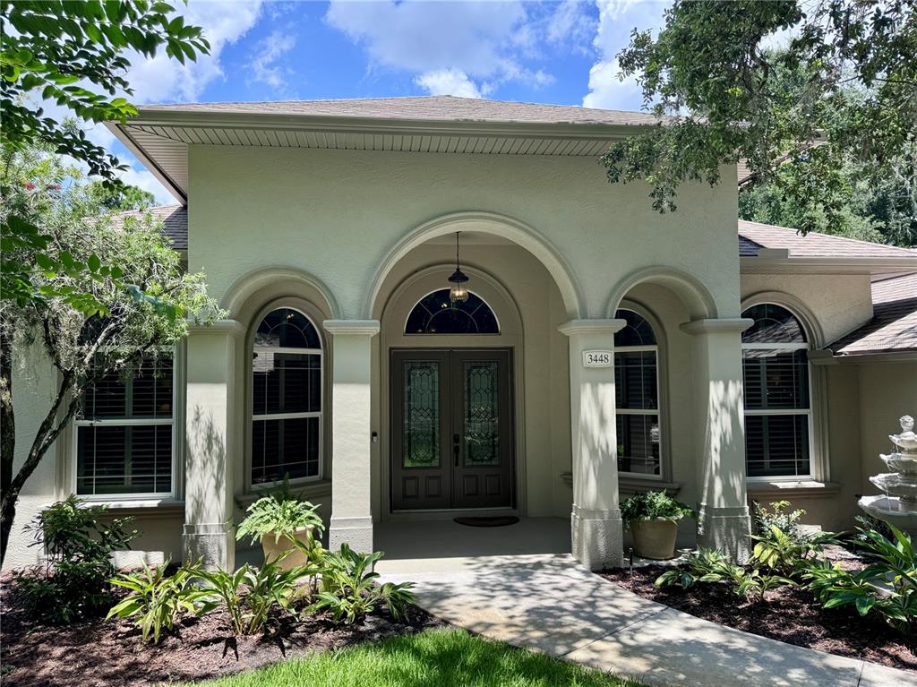 The exterior of a house features a covered arched entryway with double doors and windows — 3448 ACOMA DRIVE, ORMOND BEACH, FL