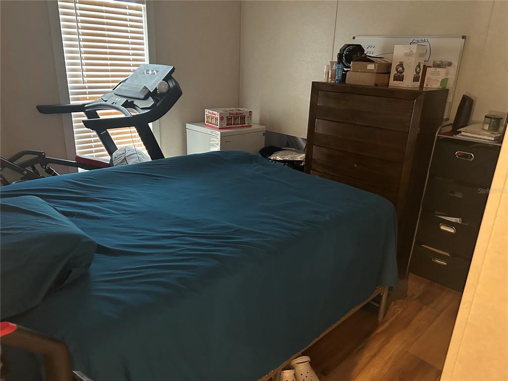A bedroom features a bed with a blue comforter, a treadmill, and dark wood furniture — 231 TANGLEWOOD DRIVE, APOPKA, FL
