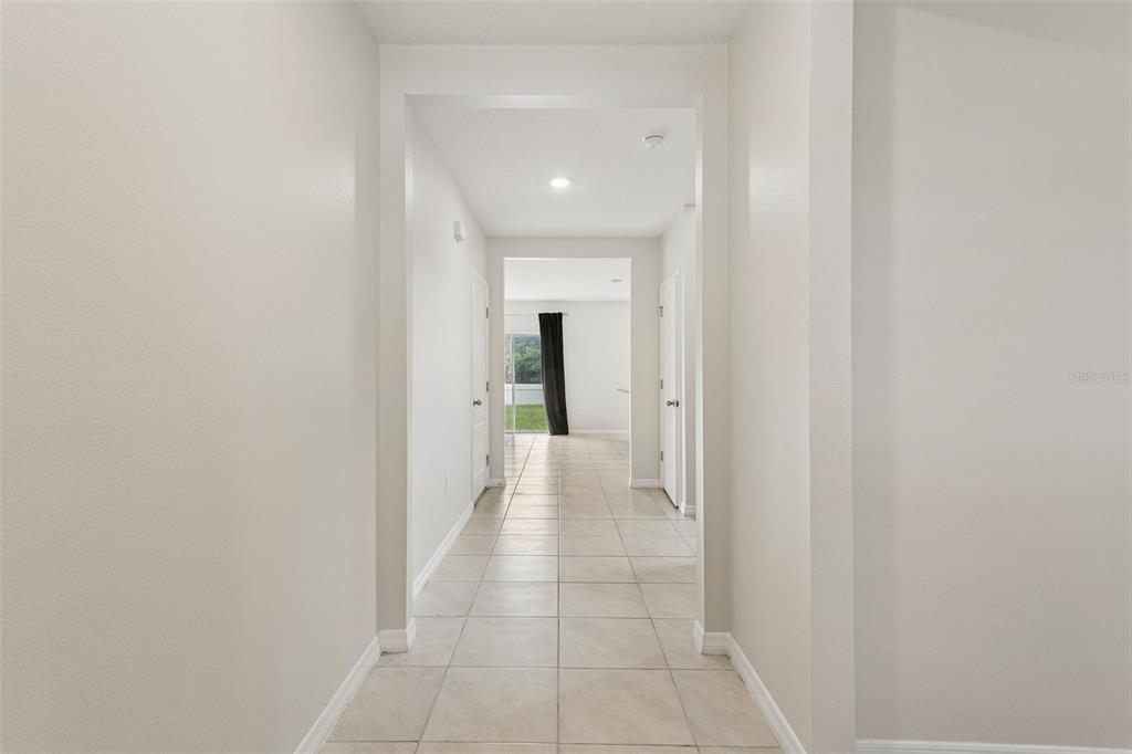 A long hallway with light-colored tile flooring leads to a room with a window — 5551 PALOMINO PLACE, APOPKA, FL