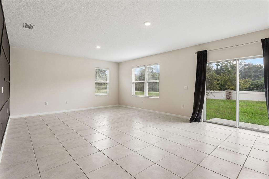 An empty living room with light tile floors, recessed lighting, and sliding glass patio doors — 5551 PALOMINO PLACE, APOPKA, FL