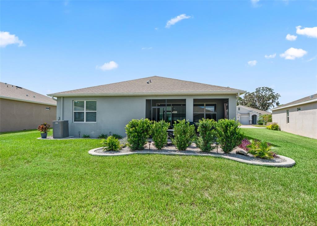 The rear exterior of a single-story house features a screened-in patio and landscaped garden bed — 5209 NW 46TH LANE RD, OCALA, FL