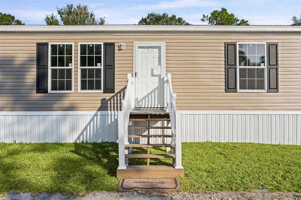 The exterior of a tan manufactured home features a white front door and wooden stairs — 8426 SWEDEN BOULEVARD, PUNTA GORDA, FL
