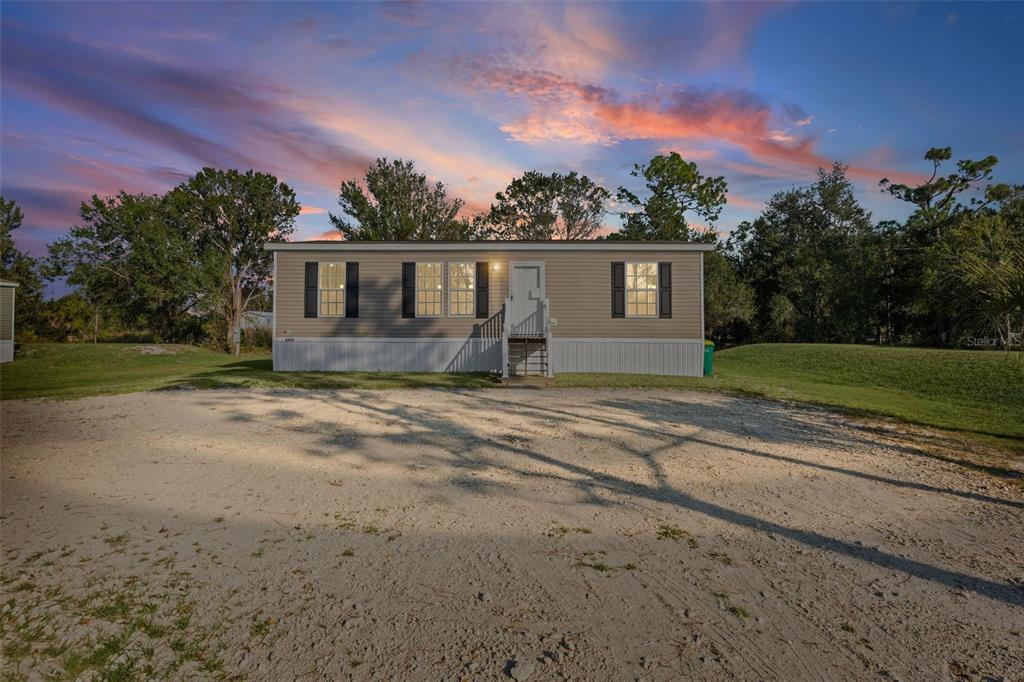 A single-story manufactured home with tan siding sits on a large dirt lot at sunset — 8426 SWEDEN BOULEVARD, PUNTA GORDA, FL