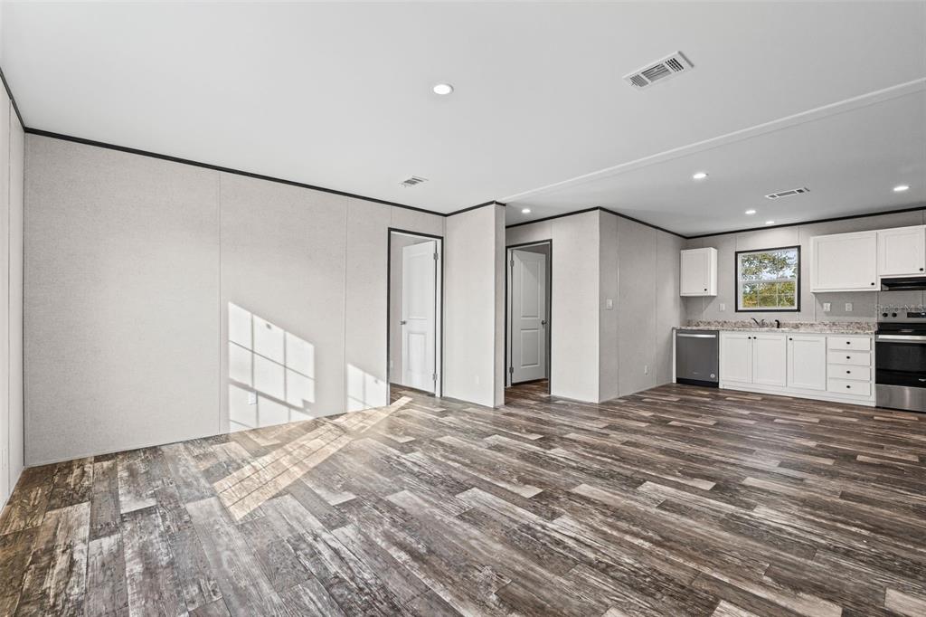 An open-concept living area features wood-look flooring, light-colored walls, and an adjacent kitchen with white cabinets — 8426 SWEDEN BOULEVARD, PUNTA GORDA, FL