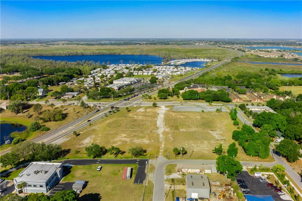 An aerial view shows a large, vacant grassy lot situated near a road and lake — 901 12TH STREET, CLERMONT, FL