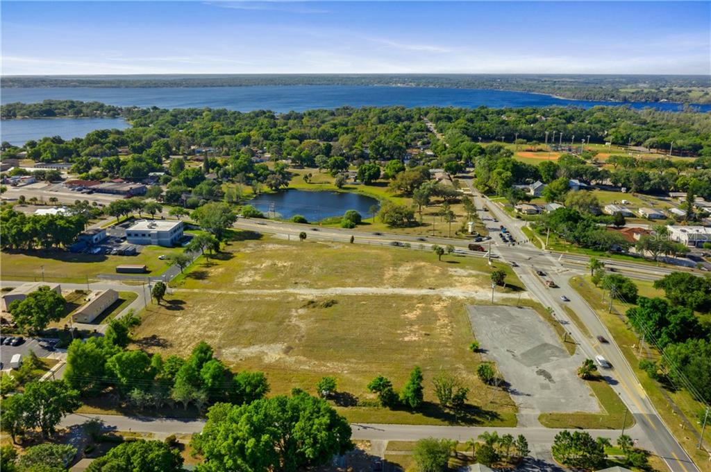 An aerial view shows a large, vacant grassy lot situated near a road and lake — 901 12TH STREET, CLERMONT, FL