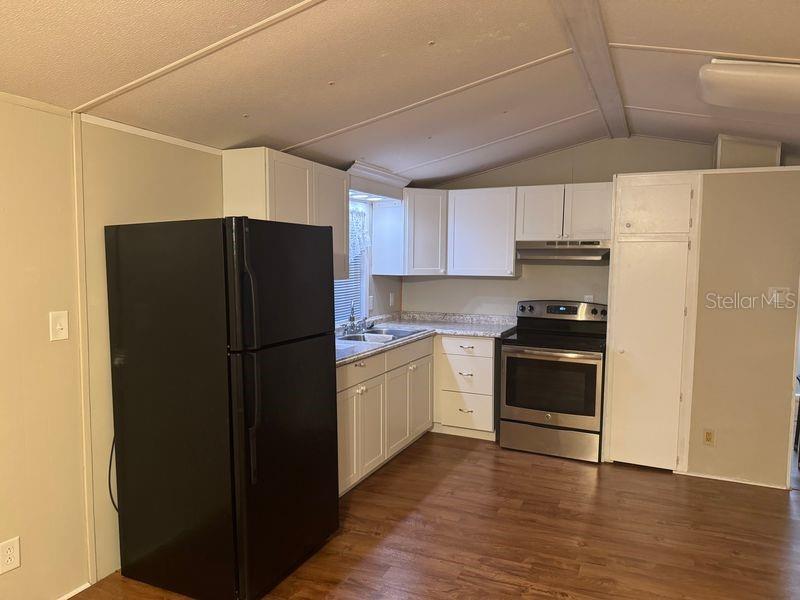 A kitchen features white cabinets, stainless steel appliances, a black refrigerator, and wood-look flooring — 7920 SUNRUNNER ROAD, NEW PORT RICHEY, FL