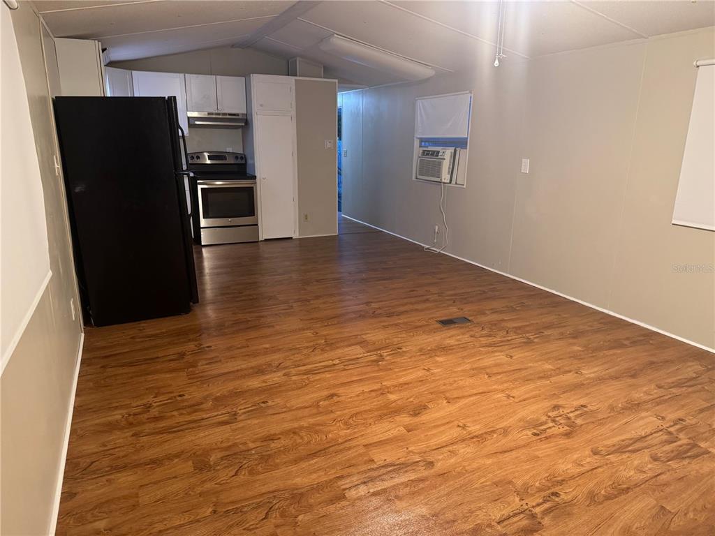 An open-concept living area features wood-look flooring, a black refrigerator, and a stainless steel stove — 7920 SUNRUNNER ROAD, NEW PORT RICHEY, FL