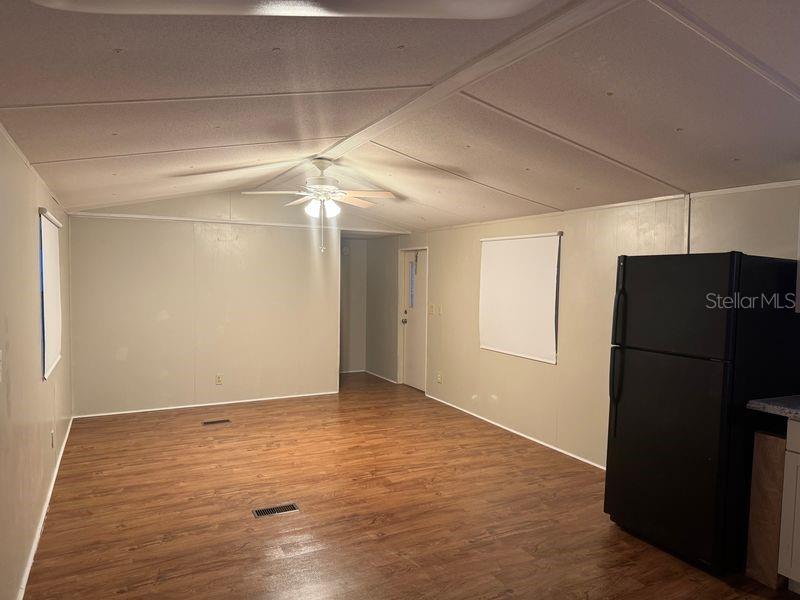 A room with wood-look flooring, a ceiling fan, and a black refrigerator — 7920 SUNRUNNER ROAD, NEW PORT RICHEY, FL