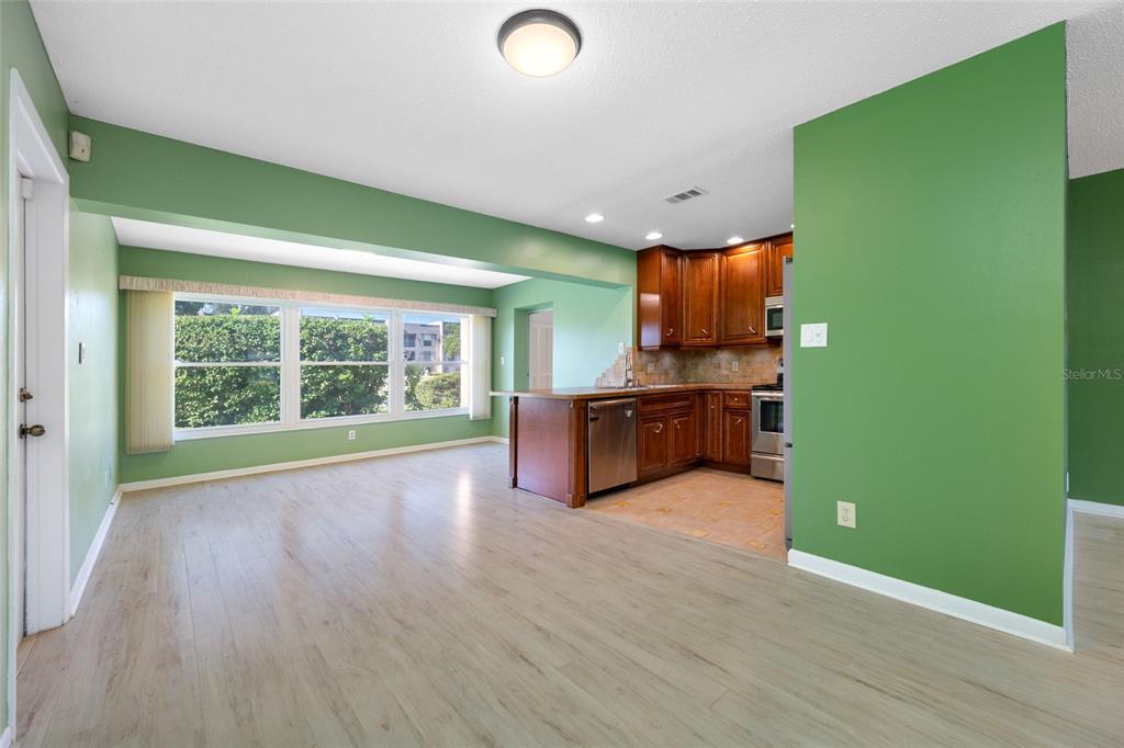 An open-concept kitchen with wood cabinets and stainless steel appliances overlooks a light-floored living area — 8440 BRENTWOOD ROAD UNIT 8440, SEMINOLE, FL