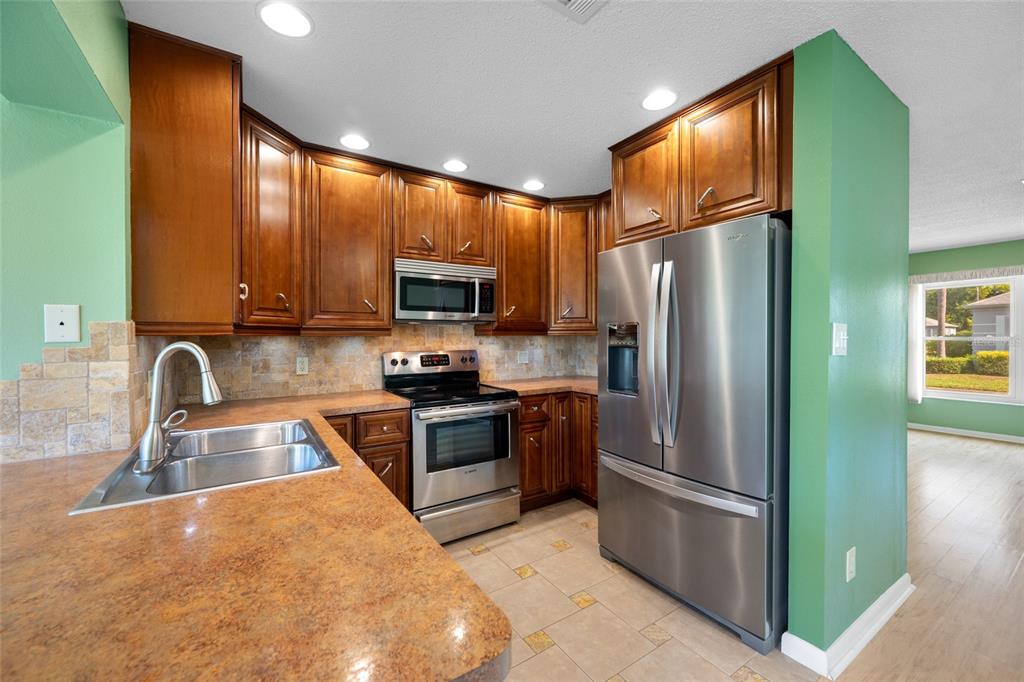 A kitchen features wood cabinets, stainless steel appliances, a stone backsplash, and a laminate countertop — 8440 BRENTWOOD ROAD UNIT 8440, SEMINOLE, FL