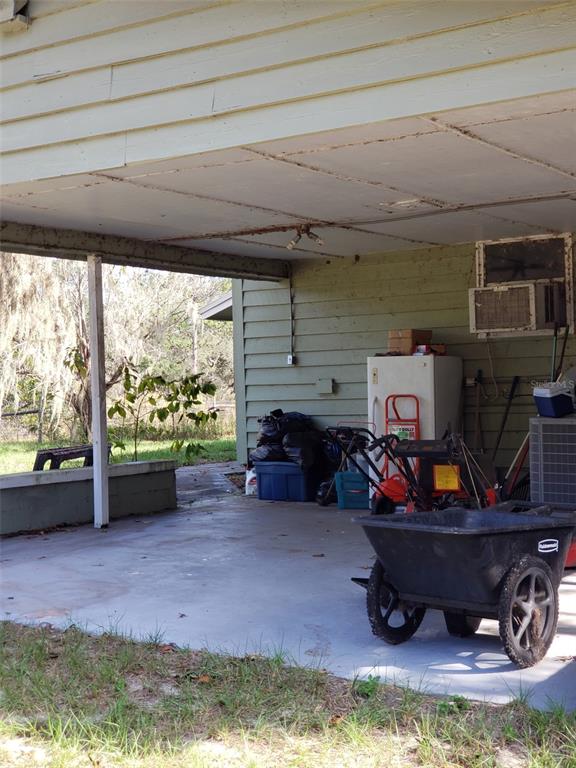 A covered concrete patio area features a white refrigerator, a wheelbarrow, and outdoor equipment — 11069 NE 14TH AVENUE, BRANFORD, FL