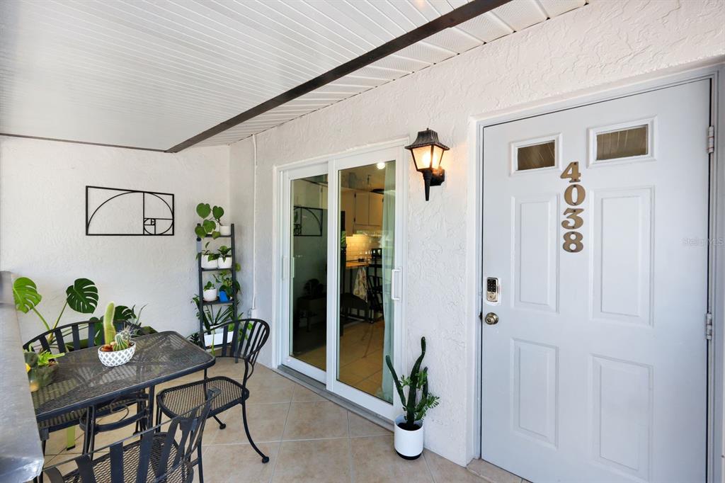 A patio features a table, chairs, potted plants, a sliding glass door, and a front door — 4038 NORTHLIGHT DRIVE UNIT 1506, NAPLES, FL