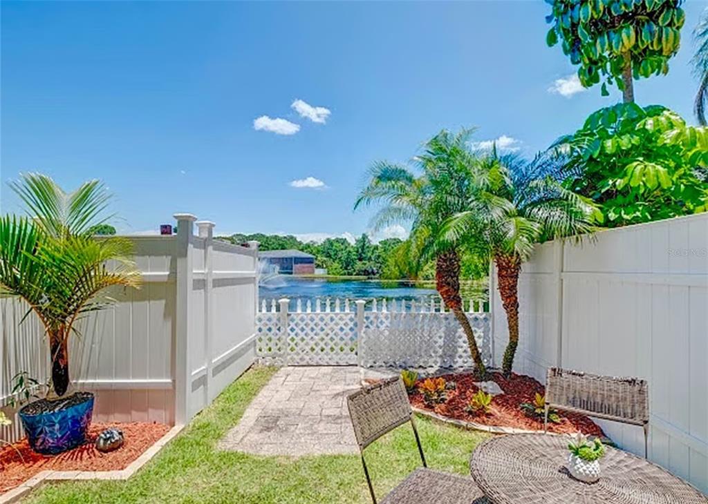 A backyard patio features a small table, two chairs, palm trees, and a white fence — 13812 ORANGE SUNSET DRIVE UNIT 0, TAMPA, FL
