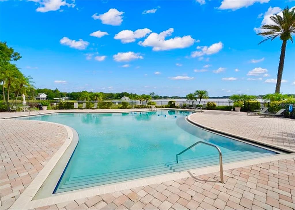 A swimming pool with a paved deck overlooks a lake under a blue sky — 13812 ORANGE SUNSET DRIVE UNIT 0, TAMPA, FL