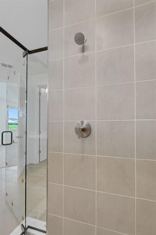 A shower with light beige square tiles, a chrome showerhead, and a glass door — 16935 SQUIRREL BRANCH LANE, ALVA, FL