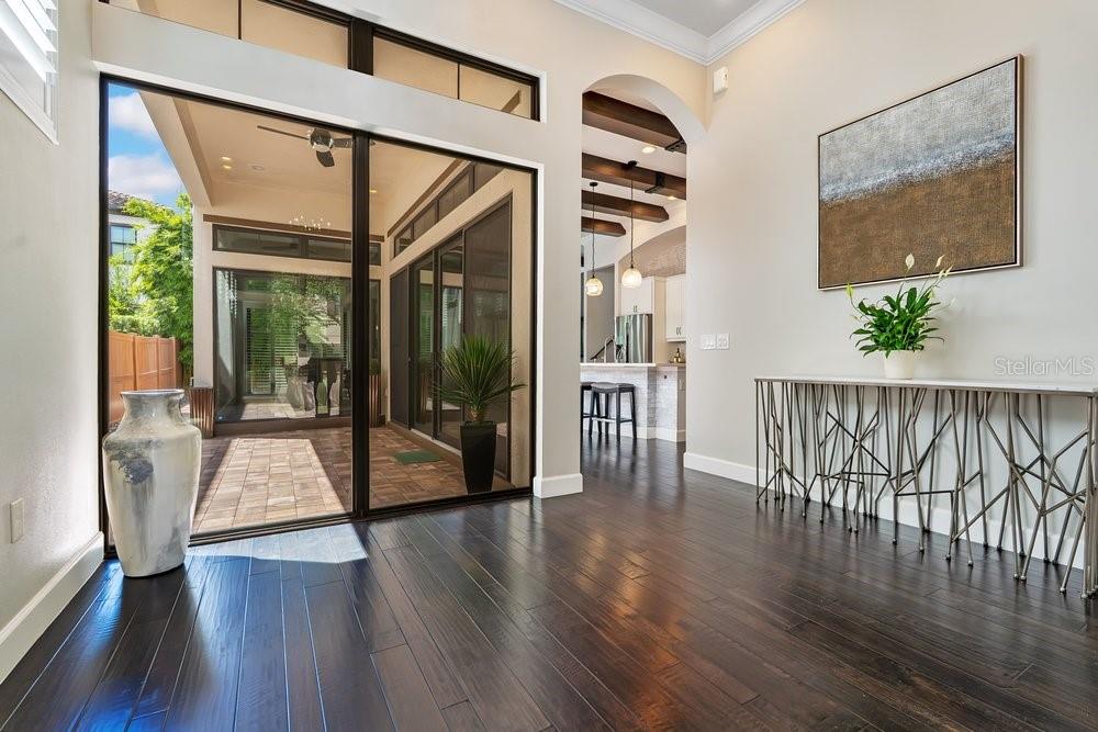 A foyer features dark hardwood floors, light gray walls, three shuttered windows, and two chandeliers — 8449 VIA VITTORIA WAY, ORLANDO, FL