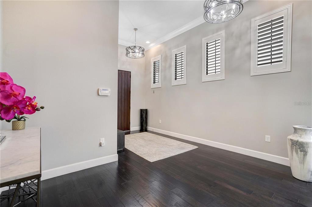 A foyer features dark hardwood floors, light gray walls, three shuttered windows, and two chandeliers — 8449 VIA VITTORIA WAY, ORLANDO, FL