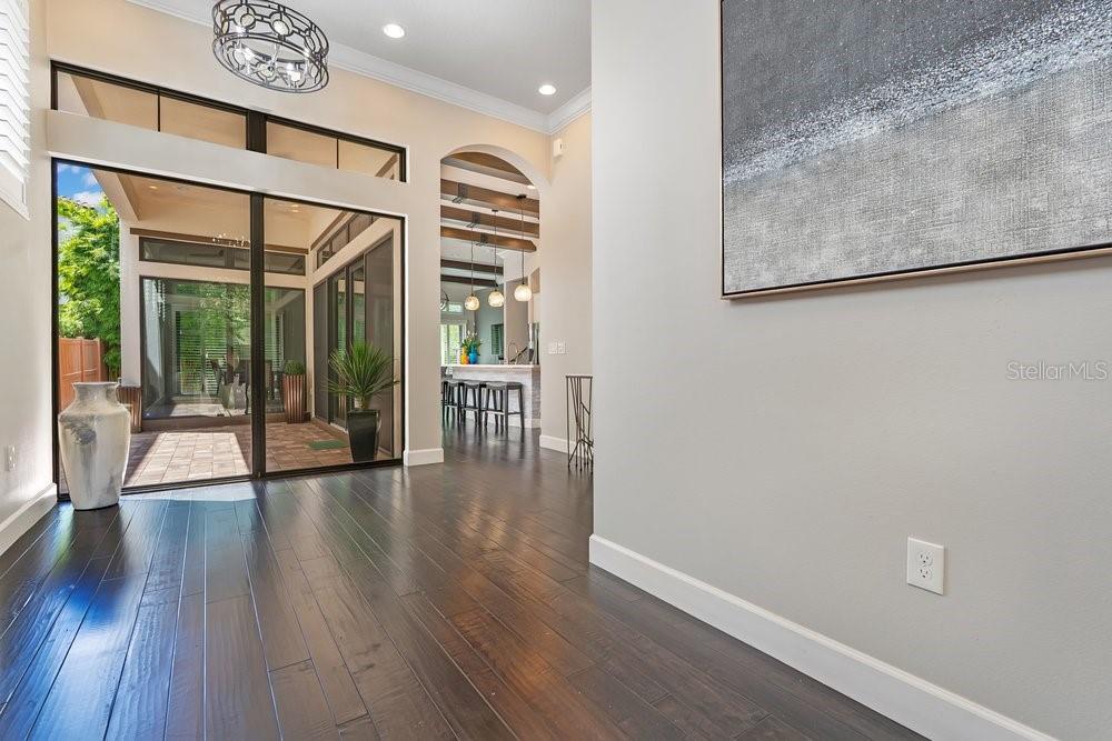 A bright entryway with dark wood floors, a console table, and sliding doors to a patio — 8449 VIA VITTORIA WAY, ORLANDO, FL