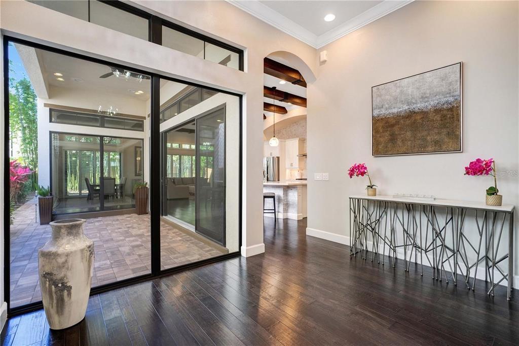 A bright entryway with dark wood floors, a console table, and sliding doors to a patio — 8449 VIA VITTORIA WAY, ORLANDO, FL
