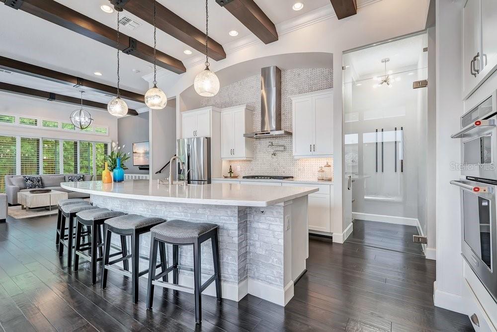 A bright kitchen features white cabinets, quartz countertops, a farmhouse sink, and dark wood beams — 8449 VIA VITTORIA WAY, ORLANDO, FL
