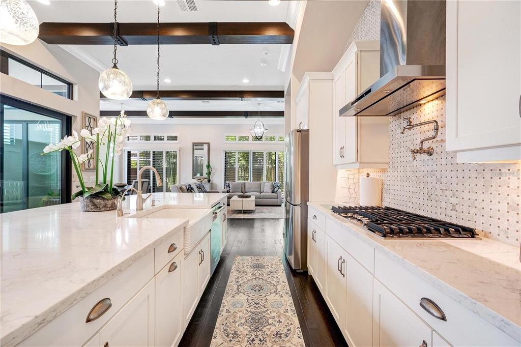 A bright kitchen features white cabinets, quartz countertops, a farmhouse sink, and dark wood beams — 8449 VIA VITTORIA WAY, ORLANDO, FL