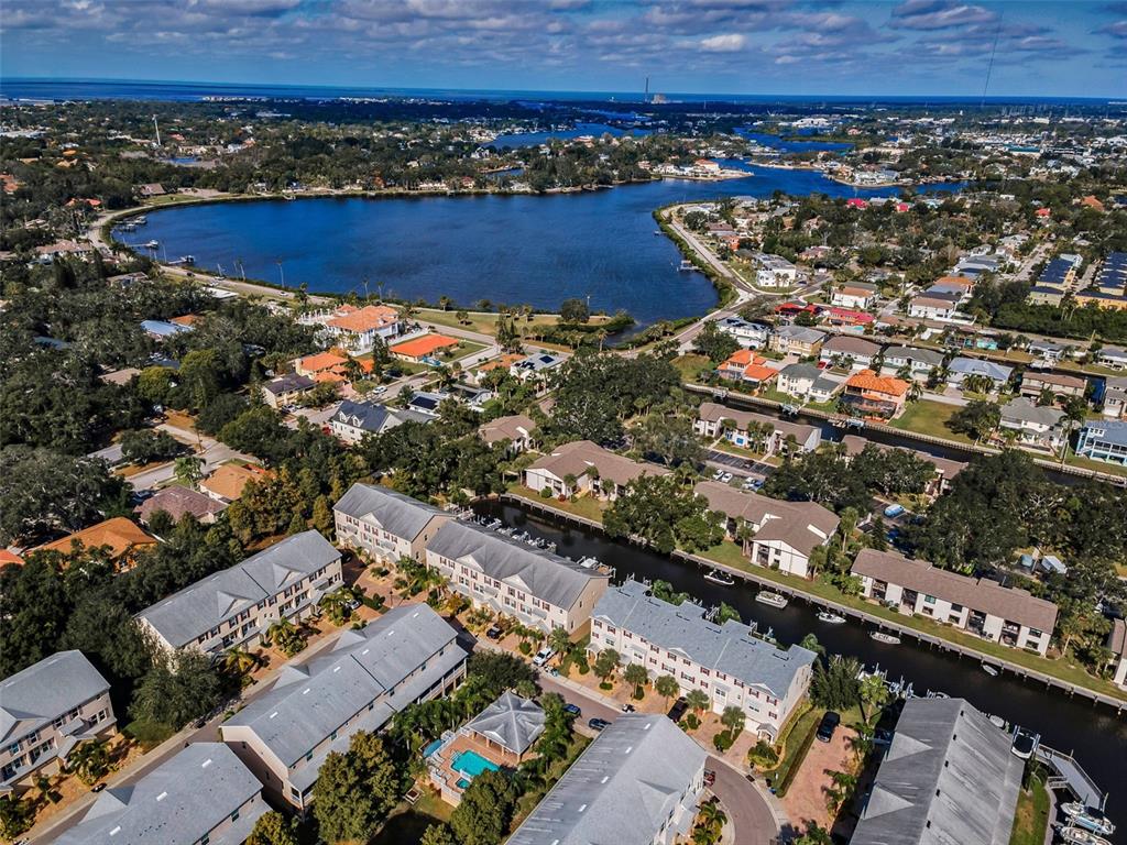 An aerial view shows multi-story residential buildings situated along a canal near a large lake — 842 CALLISTA CAY LOOP, TARPON SPRINGS, FL